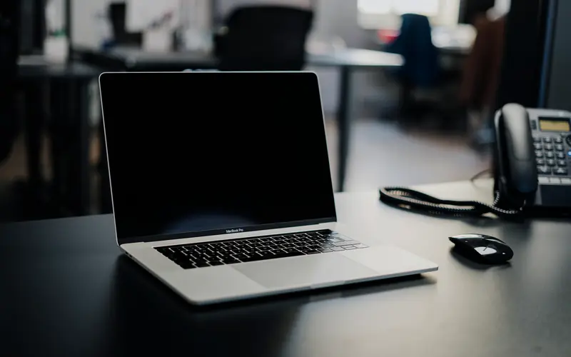 Un bureau d'accueil dans la pénombre, ordinateur portable et téléphone fixe posés sur le comptoir